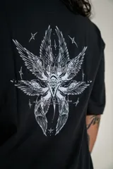 Remera oversize de algodón elastizado en color negro, con diseño gráfico estampado en la espalda que presenta motivos alados y elementos celestiales.