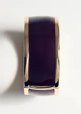 Pulsera rígida de metal dorado con esmalte negro en el centro y cierre a presión.