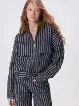 Campera de denim a rayas verticales con cuello de pana en color bordó. Presenta cierre frontal, mangas desmontables con cierre en los hombros, canesú en el pecho y bolsillos de parche cuadrados.