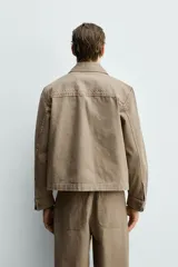 Sobrecamisa de corte boxy fit confeccionada en algodón con estructura canvas y efecto lavado. Presenta cuello solapa, cierre frontal con botones, mangas largas con puños abotonados y bolsillos de plastrón con solapa en el pecho. Incluye detalles bordados a tono en las mangas.