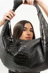 Bolso tipo hobo de cuero marrón con textura de piel de cocodrilo, asa anudada y cierre superior abierto.