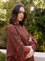 Buzo blanco de jogging sin friza, con cuello redondo y bordado floral marrón en las mangas.