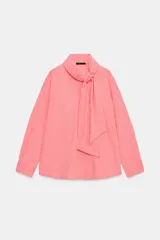 Camisa de rayas rosadas y blancas, con cuello subido decorado con un lazo integrado, manga larga con puños abotonados y cierre frontal oculto.