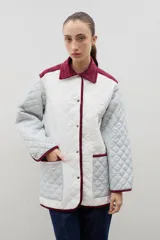 Campera acolchada de corte holgado, color blanco con diseño capitoneado en forma de rombos. Presenta cuello camisero y bordes internos con estampado floral en tonos azul y rojo, cierre frontal con botones a presión y bolsillos laterales.