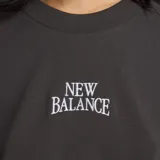 Remera New Balance de corte holgado y mangas cortas tipo raglán, color gris oscuro, con logo de la marca estampado en el centro del pecho.