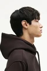 Canguro color marrón oscuro, de corte holgado, con capucha forrada y cordón ajustable. Presenta hombros caídos, bolsillo canguro y remates acanalados en puños y bajo.