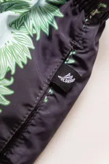 Short de baño negro con estampado de flores verdes y celestes, cintura elástica con cordón regulable, bolsillos laterales y trasero con cierre, suspensor de malla fina hipoalergénico.