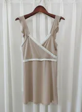 Camisón maternal color beige, con diseño de escote cruzado y breteles anchos con volados. Presenta detalles de puntilla blanca en el escote y bajo el busto, ideal para lactancia.