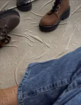 Borcego de cuero color gris con cordones color naranja, suela track negra de goma y detalle de gamuza en la parte superior del tobillo.