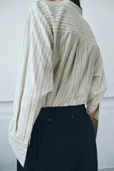 Camisa de corte oversize confeccionada en tejido con viscosa, con estampado de rayas verticales. Presenta cuello mao, cierre frontal con botones ocultos bajo solapa, mangas largas con puños anchos y bolsillos de plastrón en el delantero. El bajo es asimétrico y redondeado.