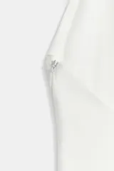 Vestido largo blanco de cuello halter con escote en V pronunciado, detalle de nudo drapeado en el delantero y tirantes decorados con cuentas esféricas.