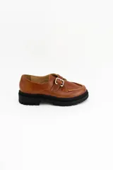 Mocasines de cuero color verde oliva con suela track negra de plataforma. Presentan una tira decorativa sobre el empeine con hebilla metálica dorada ajustable en el lateral.