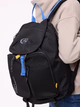 Mochila urbana marca Rusty de color negro, con múltiples compartimentos frontales, bolsillo de red lateral y detalles en azul y amarillo. Presenta el logo de la marca en la solapa superior y el texto 'Rusty Worldwide' en el frente.