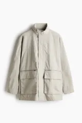 Campera parka de nylon color beige claro, con cuello elevado que oculta una capucha desplegable. Presenta cierre frontal oculto por solapa con botones a presión, bolsillos con cierre y bolsillos de solapa con botones a presión en la parte delantera, y un bolsillo interior.