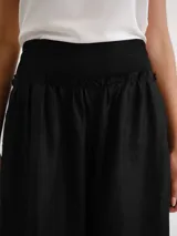 Pantalón negro de lino con cintura elástica fruncida y pernera ancha, con detalles de cordones ajustables a los lados.