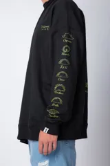 Buzo negro de corte oversize con cuello redondo y mangas largas. Presenta un pequeño logo estampado en el pecho y un diseño de empanadas y textos en la manga.