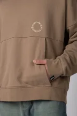 Buzo canguro oversize de frisa de algodón premium en color azul grisáceo. Presenta un diseño con recortes frontales, bolsillo tipo canguro y un pequeño logo circular estampado en el pecho. Cuenta con puños y ruedo acanalados.