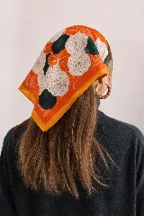 Pañuelo cuadrado de color naranja con estampado de flores blancas y verdes.