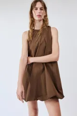 Vestido mini marrón de corte evasé con diseño tipo globo en el dobladillo, cuello redondo y mangas sisa. Presenta bolsillos laterales ocultos en la costura y cierre en la espalda con pequeña abertura y botón.