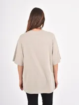 Remera de corte oversize color beige, con cuello redondo y mangas cortas. Presenta un estampado frontal con la frase 'Amore Mio', un dibujo de dos cerezas y la leyenda 'South Tuscany Italy'.