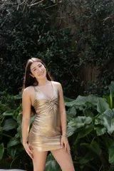 Vestido corto de fiesta color lila metalizado, con escote en V, breteles finos, cut-outs en la cintura y falda ajustada con cordones laterales.