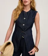 Chaleco largo de jean azul oscuro, con corte acinturado, cierre frontal abotonado y costuras con pespuntes en contraste. Presenta un diseño sin mangas con cuello redondo.