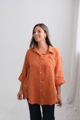Camisa de lino color terracota, de corte holgado y diseño oversize. Presenta cuello clásico, cierre frontal con botones de nácar, bolsillo en el pecho y mangas largas con sistema de ajuste mediante trabilla y botón.