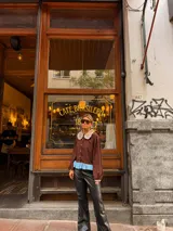 Camisa de color marrón con cuello Peter Pan en tono beige con borde de encaje, mangas largas abullonadas con puños elásticos y detalle de volado en el ruedo en color celeste.