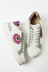 Zapatillas deportivas blancas de cuero liso, con cordones y aplique lateral con forma de ojo bordado con mostacillas de colores.