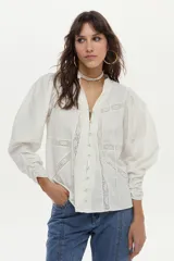 Blusa de algodón liviano color blanco, con detalles de puntilla en el frente, cuello mao con escote en V, cordón colgante y mangas largas abullonadas con puños ajustados.