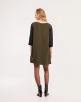 Vestido corto negro con mangas 3/4 verdes, cuello bote y bolsillos laterales.