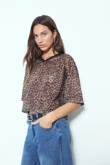 Remera de estilo deportivo con cuello en V y mangas cortas amplias. Presenta un diseño de rayas verticales en tonos marrones, blancos y líneas finas en fucsia, confeccionada en tejido de red.