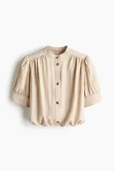 Blusa de sarga suave en color beige, con cuello mao, botonadura frontal con botones carey, mangas cortas abullonadas con puños y bajo globo.