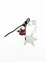Llavero decorativo con argolla metálica en forma de corazón, cordón negro y colgante en forma de estrella de mar blanca con tachas doradas, además de dijes colgantes que incluyen un corazón rojo, una bola de billar número 8 y dados.