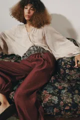 Blusa color beige confeccionada en viscosa, con cuello redondo y escote pico. Tiene mangas largas con puños y detalle de bordados con aplicación de abalorios en cuello, puños y ruedo. Diseño cruzado con fajín.