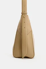 Bolso de hombro color tostado con diseño estructurado que combina paneles de cuero liso y gamuza con pespuntes visibles. Cuenta con un asa larga de hombro ajustable y cierre superior con botón imantado.