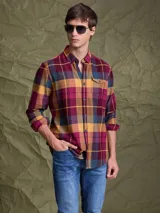 Camisa de manga larga con diseño de cuadros en tonos borravino, amarillo y azul. Presenta cuello clásico, cierre frontal con botones y un bolsillo en el pecho.