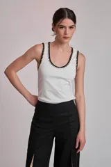 Remera negra sin mangas, tipo musculosa, con escote redondo y ribetes blancos con apliques de perlas en el contorno del cuello y las sisas.