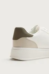 Zapatilla deportiva de diseño minimalista con parte superior lisa, suela con volumen y detalle de color a contraste en el talón.