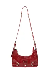 Bandolera de charol color rojo, con diseño estilo baguette. Presenta cierre superior, correas ajustables con hebillas metálicas y detalles decorativos de hebillas en la parte frontal.