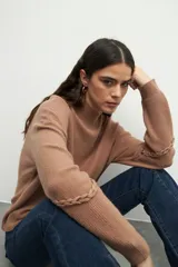 Polera color tostado de tejido de punto, con cuello alto y mangas largas abullonadas con detalle de bordado trenzado en los codos.