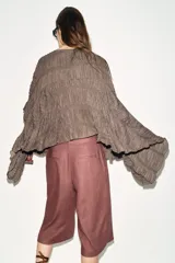 Top de cuello redondo color celeste con textura fruncida, mangas tipo capa y bajo asimétrico.