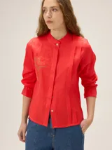 Camisa de lino rojo con cuello mao, alforzas verticales y bordado decorativo en el frente. Tiene mangas largas con volumen y puños elastizados.