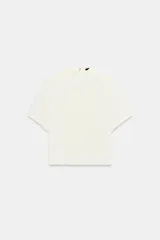 Camisa de cuello subido y manga corta con hombreras. Presenta un diseño minimalista con cierre de cremallera metálica en la espalda.