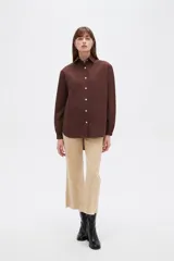 Campera marrón de manga larga confeccionada en algodón, con cuello camisero, cierre frontal con botones a presión y puños elásticos fruncidos.