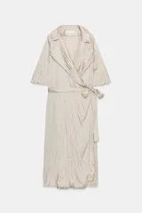 Vestido midi de Zara Woman Collection color beige, con cuello solapa, mangas por debajo del codo y diseño cruzado. Confeccionado en tejido plisado con brillo satinado, incluye un cinturón ajustable del mismo género con lazada en la cintura.