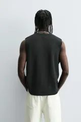 Camiseta sin mangas (tank top) negra, corte boxy fit, con cuello redondo y sisa con acabado irregular. Presenta un estampado frontal con texto manuscrito en verde y blanco que dice: "I look cool online, but offline I'm even better... Chase real likes!".