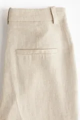 Pantalón sastrero color beige de tiro alto, confeccionado en mezcla de lino y lyocell. Presenta diseño de perneras rectas con pliegues frontales y traseros, bolsillos al bies y trabillas para cinturón.