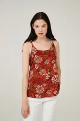 Musculosa color ladrillo con estampado de flores blancas y hojas verdes, breteles finos y escote redondo.