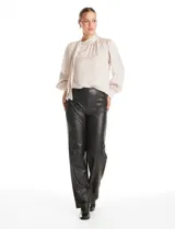 Blusa de acabado satinado color beige, con cuello alto fruncido, cierre lateral con botones y lazo decorativo. Presenta mangas largas estilo balloon con puños ajustados.
